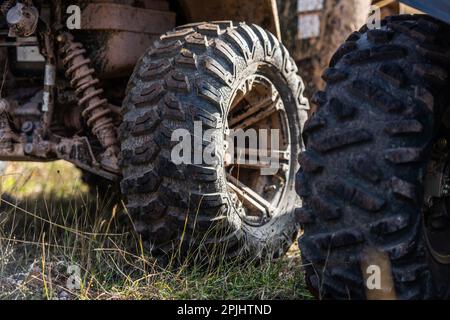 Nahaufnahme des Geländes von Quad Bike auf unbefestigten Landstraßen. Verschmutztes Rad eines Geländefahrzeugs mit Allradantrieb. Reise- und Abenteuerkonzept. Stockfoto