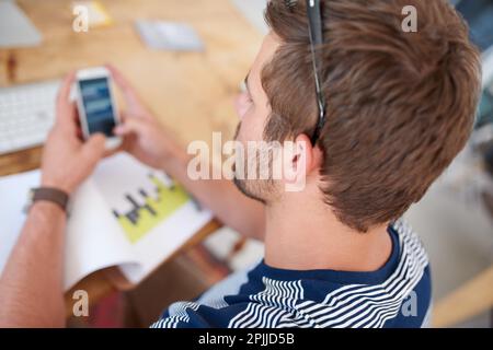 Mit der notwendigen Technologie arbeiten. Draufsicht über die Schulter eines jungen Mannes, der sich Informationen auf seinem Mobiltelefon ansieht. Stockfoto