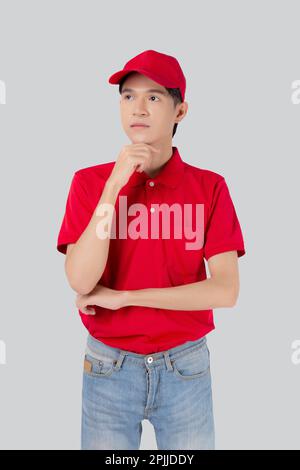 Junger asiatischer Mann in Uniform Rot und Mütze Standing und Denkweise isoliert auf weißem Hintergrund, Mitarbeiter oder Händler, Kurier und Zusteller, Lieferer Stockfoto