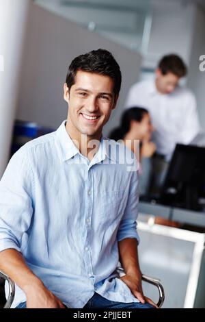 Er ist glücklich, wo er ist. Porträt eines selbstbewussten jungen Geschäftsmannes mit seinen Kollegen verschwommen im Hintergrund. Stockfoto