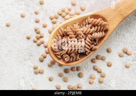 Grüne Fusilli-Nudeln mit Linsen auf grauem Betonhintergrund. Ein Löffel rohe Pasta und grüne Linsen. Glutenfreie Pasta. Stockfoto