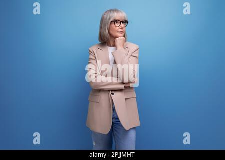 60s reife Frau in Geschäftskleidung steht mit Bedacht auf einem Studiohintergrund mit Kopierbereich Stockfoto