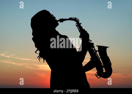 Silhouette einer Frau, die bei Sonnenuntergang Saxophon gegen den wunderschönen Himmel spielt Stockfoto