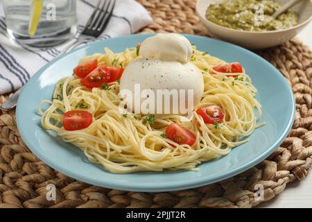 Teller mit köstlicher Pasta mit Burrata und Tomaten auf Korbmatte Stockfoto