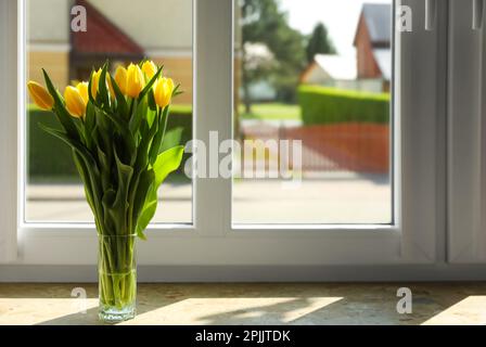 Blumenstrauß mit wunderschönen gelben Tulpenblumen in Glasvase auf Fensterbank. Platz für Text Stockfoto