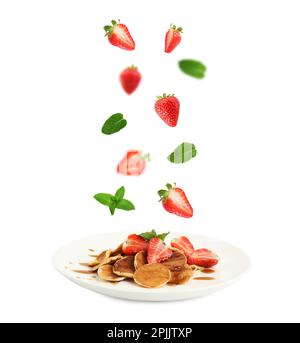 Frische Erdbeeren und Minzblätter, die vor weißem Hintergrund auf Pfannkuchen fallen Stockfoto