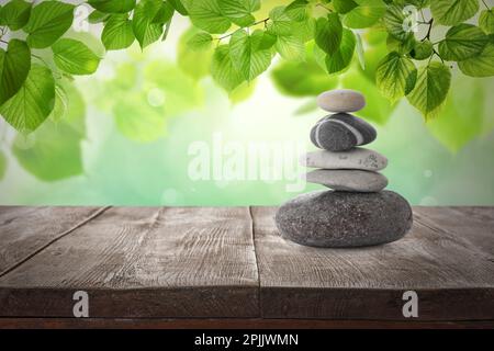 Gestapelte Steine auf einem Holztisch unter grünen Blättern vor verschwommenem Hintergrund, Platz für Text. Zen-Konzept Stockfoto