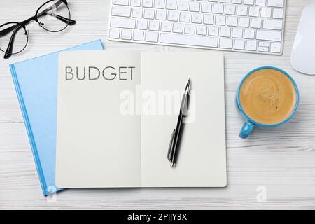 Notizbuch mit Wort Budget, Computertastatur und Tasse Kaffee auf weißem Holzschreibtisch, flach liegend Stockfoto