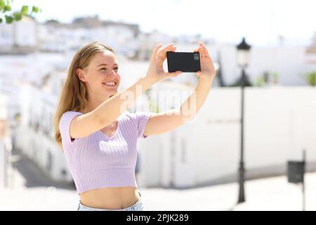 Glücklicher Teenager, der in einer weißen Straße Schlappschwanz macht oder ein Foto macht Stockfoto