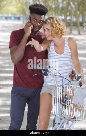 Ein Mann telefoniert mit einem Smartphone, während eine Frau auf dem Fahrrad sitzt Stockfoto