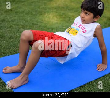 Asiatisch kluges Kind, das Yoga macht, im Gesellschaftspark draußen, Kinder Yoga Pose. Der kleine Junge, der Yoga macht Stockfoto