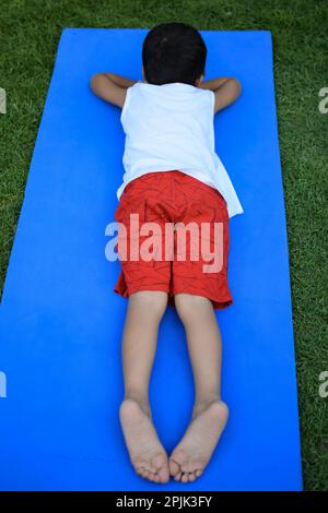 Asiatisch kluges Kind, das Yoga macht, im Gesellschaftspark draußen, Kinder Yoga Pose. Der kleine Junge, der Yoga macht Stockfoto