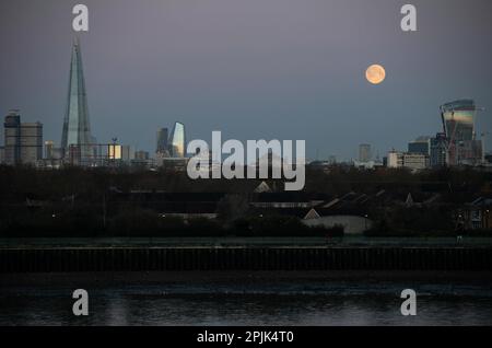 Die Skyline von London, wenn der Mond früh am Morgen untergeht, mit Blick auf die Themse. Der Wurmmond des März geht unter, genau wie die Sonne anfängt Stockfoto