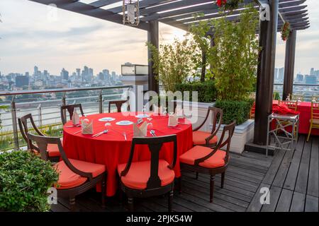 Phnom Penh, Kambodscha-Dezember 24. 2022: Leuchtend rote Tischdecke, die über einer runden Holztischplatte hängt, mit silbernem Besteck, Tellern und Servietten und Stockfoto