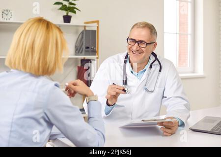 Der glückliche Senior Doktor redet über etwas Lustiges mit seiner weiblichen Patientin Stockfoto