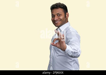 Das Porträt eines lächelnden indianers zeigt das Zeichen "OK". Hintergrund in Pastellbeige. Stockfoto