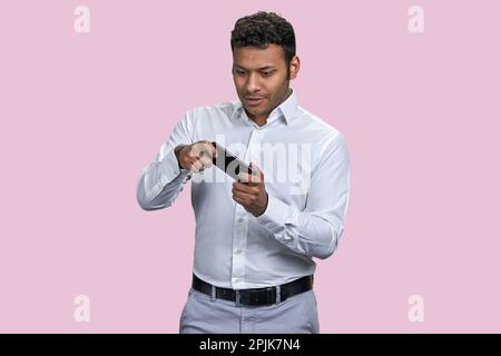 Aufgeregter, glücklicher, junger indianer, der ein Spiel mit dem Smartphone spielt. Mobile Videospiel-App. Isoliert auf pinkfarbenem Hintergrund. Stockfoto