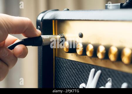 Mann, steck einen Stecker in einen Gitarrenverstärker, geringe Schärfentiefe Stockfoto