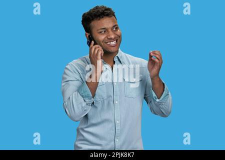 Ein junger, fröhlicher araber spricht am Handy. Isoliert auf blauem Hintergrund. Stockfoto