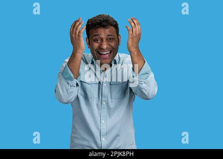 Der junge araber sieht sich etwas Lächerliches an und lacht. Isoliert auf blau. Stockfoto
