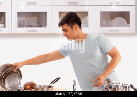 Junger Mann, der nach dem Waschen in der Küche Geschirr aufstellt Stockfoto