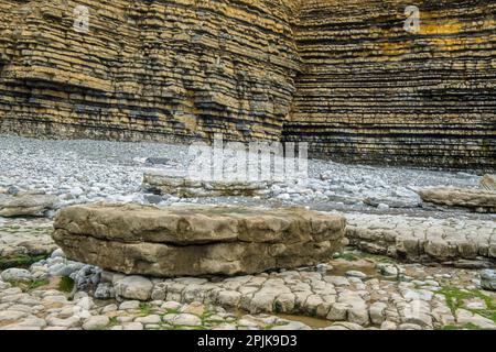 Kalksteinklippen in Schichten mit rocka und Kieselsteinen unten an der Dunraven Bay am vereinbarten Aprilnachmittag am Vale of Glamorgan und Glamorgan Heritage Coast Stockfoto