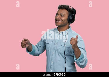 Lächelnder, fröhlicher Indianer, der Musik über Kopfhörer hört. Isoliert auf pinkfarbenem Hintergrund. Stockfoto