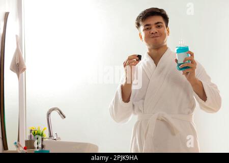 Junger Mann spült Mund mit Mundwasser im Badezimmer Stockfoto