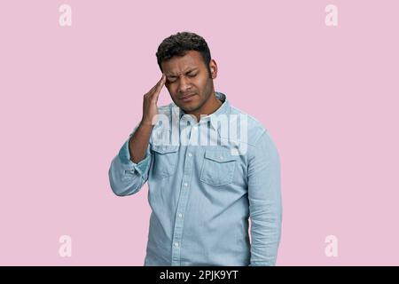 Gestresster indischer Mann mit Kopfschmerzen oder Migräneschmerzen. Isoliert auf Pink. Stockfoto
