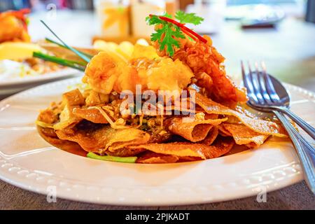 Gebratenes, knuspriges, gebratenes Wonton Pad thai im thailändischen Stil mit Garnelen oder Garnelen, Bohnensprossen, Chili in weißer Keramikplatte auf einem Holztisch. Stockfoto