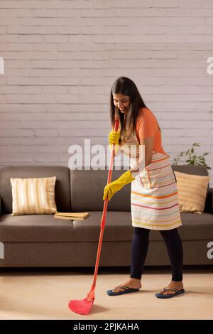 Porträt einer Frau, die zu Hause mit einem Besen den Boden fegt Stockfoto