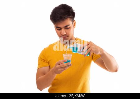 Junger Mann, der vor weißem Hintergrund Mundwasser eingießt Stockfoto