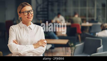 Porträt einer erfolgreichen Managerin, die im Büro mit wechselnden Händen im Hintergrund von Kollegen steht Stockfoto