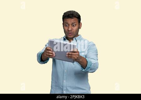 Porträt eines schockierten inders, der sich auf einem Tablet-pc etwas Ungewöhnliches ansieht. Isoliert auf weißem Hintergrund. Stockfoto