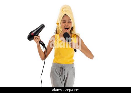 Ein Mädchen singt mit Fön und Haarbürste vor weißem Hintergrund Stockfoto