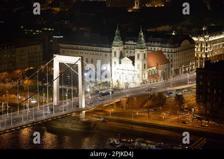 Naher Blick aus dem Hochwinkel bei Nacht in Richtung Stadtgemeindekirche, Elisabethbrücke und Platz vom 15. März vom Gellert-Hügel in Budapest, Ungarn. Stockfoto