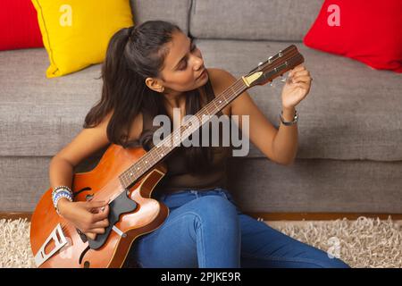 Junge Frau, die Gitarre spielt, während sie im Wohnzimmer sitzt Stockfoto