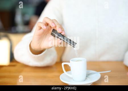 Nahaufnahme des Porträts einer Frau, die Zucker in eine Kaffeetasse in einer Bar wirft Stockfoto