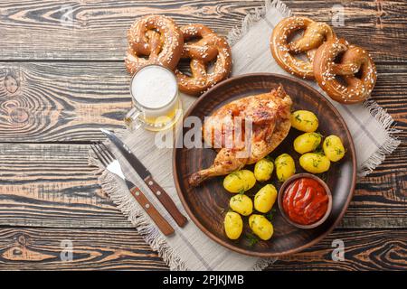 Gegrilltes Hähnchen mit gekochten Kartoffeln und Tomatensauce, serviert mit Bier und Brezeln auf dem Holztisch. Horizontale Draufsicht von oben Stockfoto