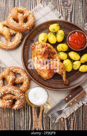 Oktoberfest Roast Chicken Wiesn Hendl mit Kartoffeln serviert mit Bier und Brezel Nahaufnahme auf dem Holztisch. Vertikale Draufsicht von oben Stockfoto