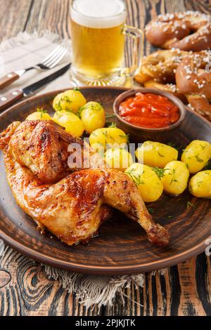 Deutsches Festtagsessen, halb gebratenes Hähnchen mit gekochten Kartoffeln, Soße, Bier und Brezeln, dicht auf einem Holztisch. Vertikal Stockfoto