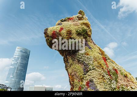 Bilbao, Spanien - September 2022: Hündchen, die von Jeff Koons und dem Iberdrola-Turm entworfene blumige Hundeskulptur an einem sonnigen Tag Stockfoto