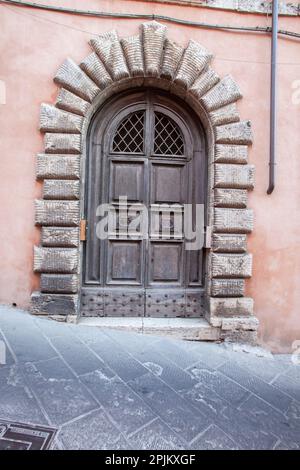 Italien, Umbrien. Alte Holztür umgeben von einem Steinbogen in der historischen Stadt Todi. Stockfoto