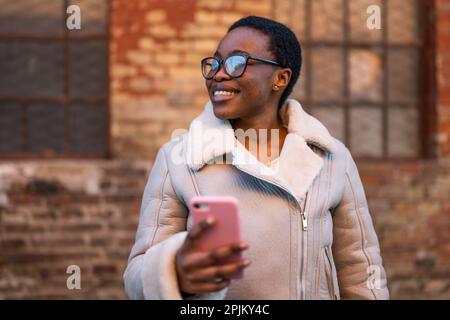 Außenporträt einer glücklichen afroamerikanischen Frau. Sie verwendet ein Smartphone. Stockfoto