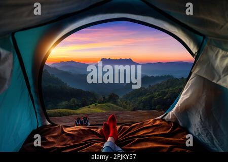 Frau überquert Bein auf Decke im Campingzelt mit Schlafsäcken auf Bergsteigen. Blick von innen auf die Berge von Doi luang chiang dao. Stockfoto