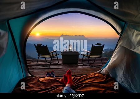 Frau überquert Bein auf Decke im Campingzelt mit Schlafsäcken auf Bergsteigen. Blick von innen auf die Berge von Doi luang chiang dao. Stockfoto