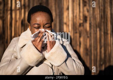 Außenporträt einer afroamerikanischen Frau. Sie bläst sich die Nase. Stockfoto