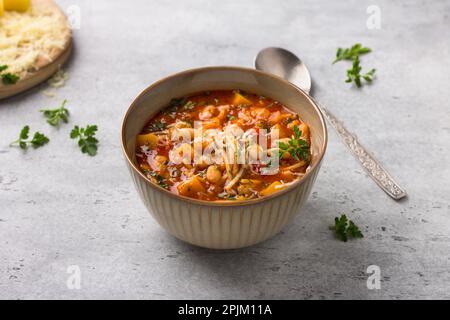 Vegane italienische Minestronsuppe der Saison mit Kürbis, Bohnen, Tomaten, Paprika, Pasta und Kräutern auf grauem, strukturiertem Hintergrund. Köstliche hausgemachte FO Stockfoto