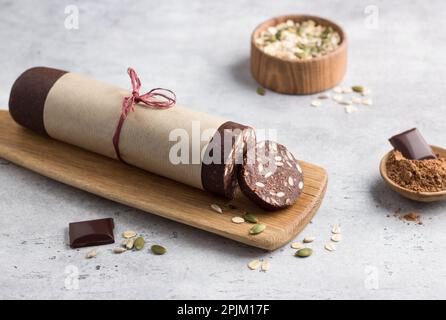 Schokoladenwurst mit Haferbrei und Samen auf grauem, strukturiertem Hintergrund. Köstliches, gesundes veganes Dessert Stockfoto