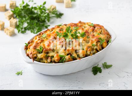 Vegetarische Füllung mit Kürbis, knusprigen Croutons, Lauch, Sellerie und Käse in einer weißen Keramikform auf hellgrauem, strukturiertem Hintergrund. Traditionell Stockfoto